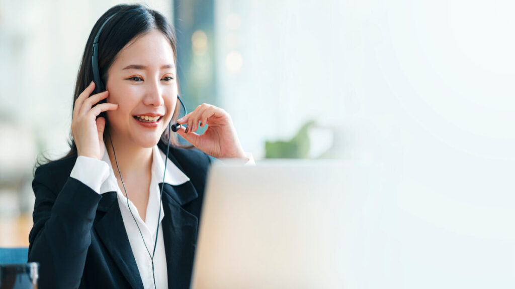 Female call center or customer support agent in broaden view panorama wearing headset while working at office to support remote customer, video conference call.